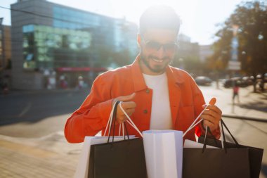 Smiling man with shopping bags walking down the street. Purchases, black friday, discounts, sale concept. 