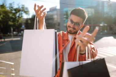 Alışveriş torbalarıyla sokakta yürüyen gülümseyen adam. Satın almalar, Kara Cuma, indirimler, satış konsepti. 
