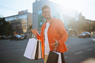 Alışveriş torbalarıyla sokakta yürüyen gülümseyen adam. Satın almalar, Kara Cuma, indirimler, satış konsepti. 