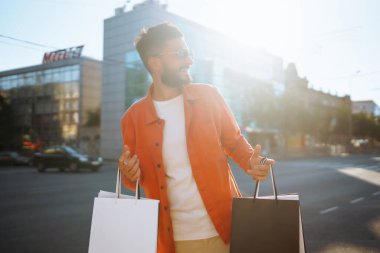 Alışveriş torbalarıyla sokakta yürüyen gülümseyen adam. Satın almalar, Kara Cuma, indirimler, satış konsepti. 