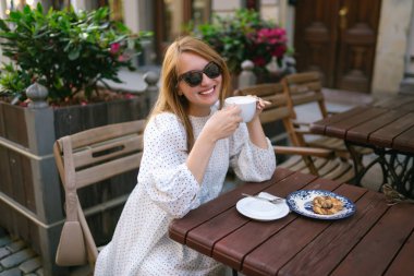 Güzel bir kadın, şehir caddesinde rahat bir kafede kahve içer. İnsanlar, moda, yaşam tarzı, seyahat ve tatil kavramı