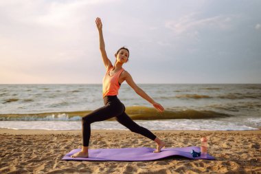 Yoga in the morning. Young woman in sportswear doing fitness exercise on the beach. Calmness and balance, a healthy lifestyle.