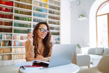 Çevrimiçi konferans, eğitim. Dizüstü bilgisayarla çalışan genç kız, üniversite kütüphanesinde öğreniyor. Serbest Çalışan, İş, Eğitim Konsepti.