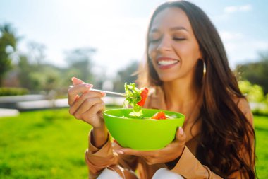 Güneşli bir günde dışarıda taze sebze salatası yiyen güzel bir kadın. Sağlıklı bir yaşam tarzı. Kavramsal piknik. Vejetaryen.