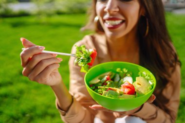 Güneşli bir günde dışarıda taze sebze salatası yiyen güzel bir kadın. Sağlıklı bir yaşam tarzı. Kavramsal piknik. Vejetaryen.