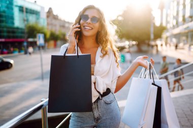 Young woman with shopping bags walking on street.  Consumerism, sale, purchases, shopping, lifestyle concept.
