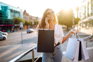 Alışveriş torbalarıyla sokakta yürüyen genç bir kadın. Tüketim, satış, alım, alışveriş, yaşam tarzı konsepti.