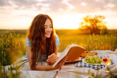 Beautiful young woman having picnic  in park. Summer picnic in nature. Healthy food. People, lifestyle, relaxation and vacations concept.