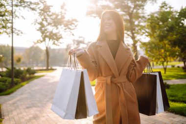 Smiling woman with shopping bags walking down the street. Purchases, black friday, discounts, sale concept. Autumn shopping.