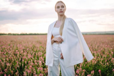 Young woman in stylish summer dress feeling free in the field with flowers. Nature, fashion, vacation and lifestyle