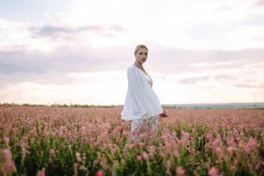 Young woman in stylish summer dress feeling free in the field with flowers. Nature, fashion, vacation and lifestyle