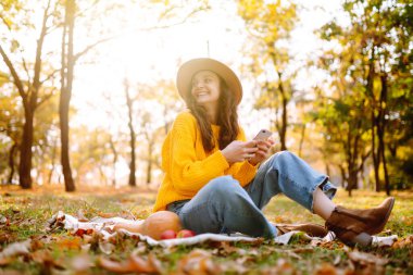 Fall picnic with pumpkin. Stylish woman enjoying autumn weather in the park. People, lifestyle, relaxation and vacations concept. Autumn harvest.