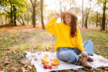 Fall picnic with pumpkin. Stylish woman enjoying autumn weather in the park. People, lifestyle, relaxation and vacations concept. Autumn harvest.