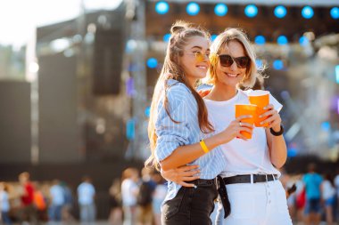 Two young woman  having a great time at a music festival. Happy girlfriends rinking beer and having fun at Beach party. Summer holiday, vacation concept.