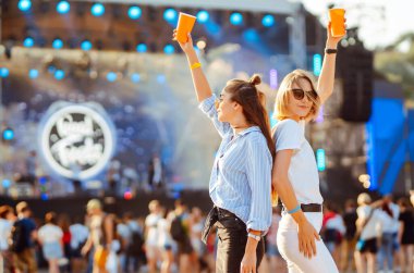 Two young woman  having a great time at a music festival. Happy girlfriends rinking beer and having fun at Beach party. Summer holiday, vacation concept.