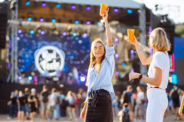 Two young woman  having a great time at a music festival. Happy girlfriends rinking beer and having fun at Beach party. Summer holiday, vacation concept.