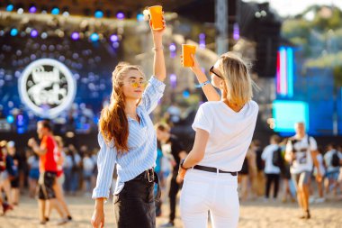Two young woman  having a great time at a music festival. Happy girlfriends rinking beer and having fun at Beach party. Summer holiday, vacation concept.