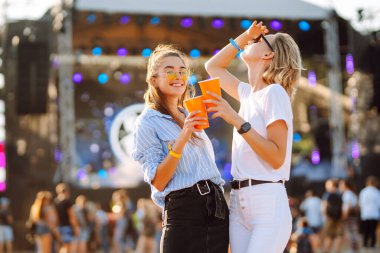 Two young woman  having a great time at a music festival. Happy girlfriends rinking beer and having fun at Beach party. Summer holiday, vacation concept.