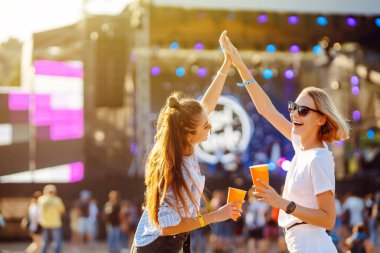 Two young woman  having a great time at a music festival. Happy girlfriends rinking beer and having fun at Beach party. Summer holiday, vacation concept.