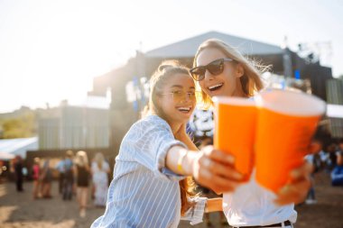 Two young woman  having a great time at a music festival. Happy girlfriends rinking beer and having fun at Beach party. Summer holiday, vacation concept.