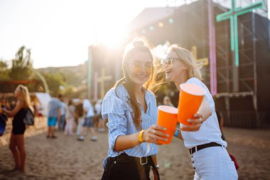 Two young woman  having a great time at a music festival. Happy girlfriends rinking beer and having fun at Beach party. Summer holiday, vacation concept.