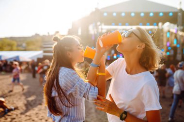 Two young woman  having a great time at a music festival. Happy girlfriends rinking beer and having fun at Beach party. Summer holiday, vacation concept.