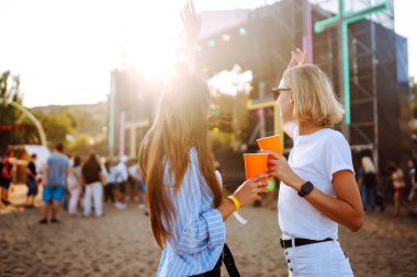 Two young woman  having a great time at a music festival. Happy girlfriends rinking beer and having fun at Beach party. Summer holiday, vacation concept.