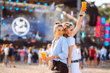 Two young woman  having a great time at a music festival. Happy girlfriends rinking beer and having fun at Beach party. Summer holiday, vacation concept.