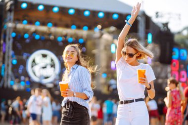 Two young woman  having a great time at a music festival. Happy girlfriends rinking beer and having fun at Beach party. Summer holiday, vacation concept.