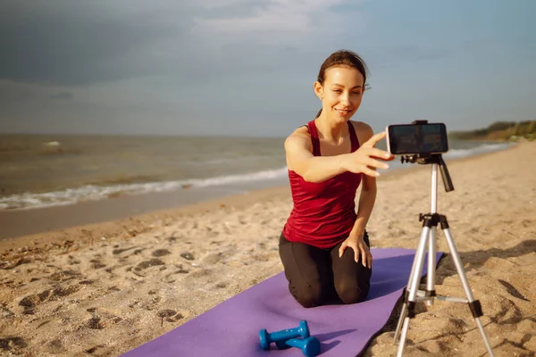 Online training. Young sporty woman yoga coach records video online training yoga on the beach. Sport, Active life, blogging.