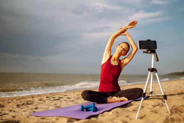 Online training. Young sporty woman yoga coach records video online training yoga on the beach. Sport, Active life, blogging.