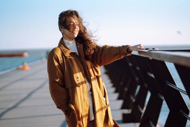 Young woman on the pier enjoying autumn weather. People, lifestyle, relaxation and vacations concept.