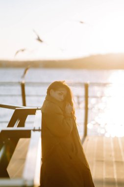 Young woman on the pier enjoying autumn weather. People, lifestyle, relaxation and vacations concept.