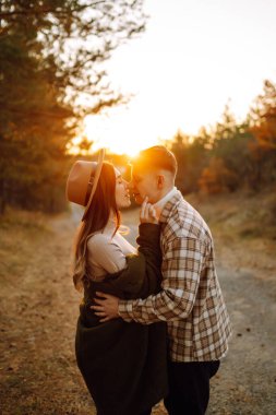 Günbatımında genç çift sonbahar parkında yürüyüp sarılıyor. İnsanlar, yaşam tarzı, rahatlama ve tatil kavramı.