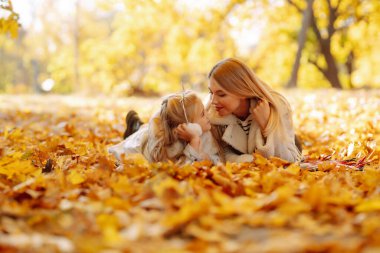 Genç anne ve kızı parkta yürüyor ve güzel sonbahar doğasının tadını çıkarıyorlar. Dinlen, çocukluk, yürüyüş, aile.