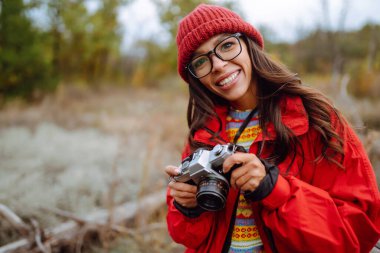 Genç bir kadın, sonbahar ormanında fotoğraf çeken bir turist. Dinlenme, rahatlama, turizm, doğa, yaşam tarzı konsepti.