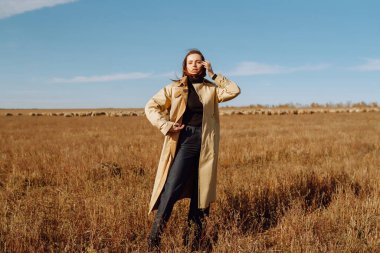 Sonbahar tarlasında poz veren şık elbiseli genç bir kadın. Doğa, moda, tatil ve yaşam tarzı. Seyahat ve macera.