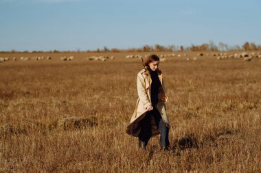 Sonbahar tarlasında poz veren şık elbiseli genç bir kadın. Doğa, moda, tatil ve yaşam tarzı. Seyahat ve macera.