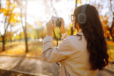 Genç bir kadın sonbahar ormanında fotoğraf çekiyor. Sarı Yeşilliklerle Sonbahar Parkı 'nda Yürüyen Kadın.