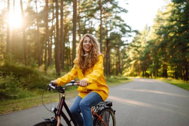 Sonbahar parkında bisiklete binen sarı montlu güzel mutlu kadın. Sonbahar modası. Yaşam tarzı. Rahatla, doğa kavramı..