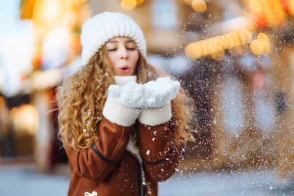 Close up Hands in warm mittens make snow in winter. Happy young woman in snowy winter park. Cold weather. Holidays, rest, travel concept.