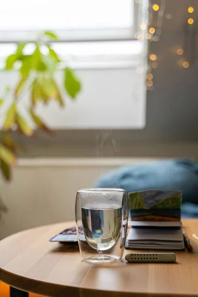 Copa de vidrio de agua caliente en mesa de madera con dibujo de acuarela en cuaderno de papel Imagen de stock