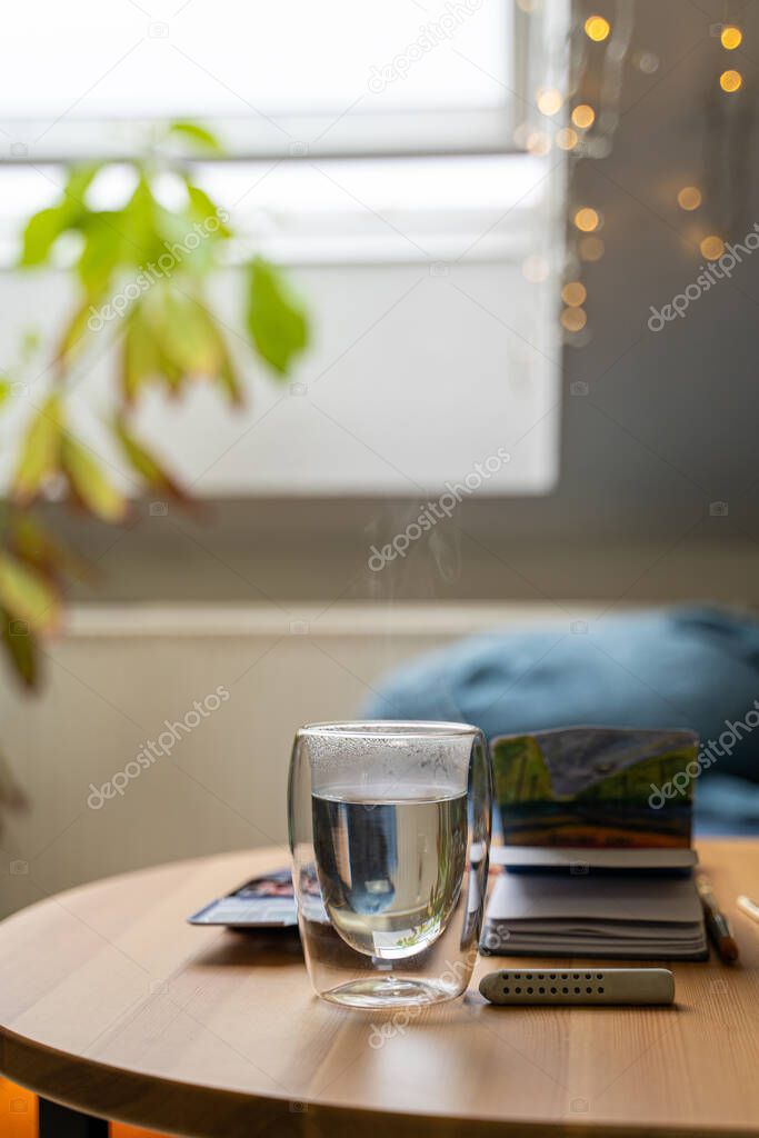 Glass cup of hot water on wooden table with watercolor drawing in paper notebook