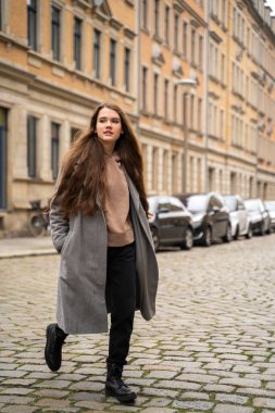 Genç esmer kadın gündüz vakti sokak yolunda günlük kıyafetlerle dolaşıyor.