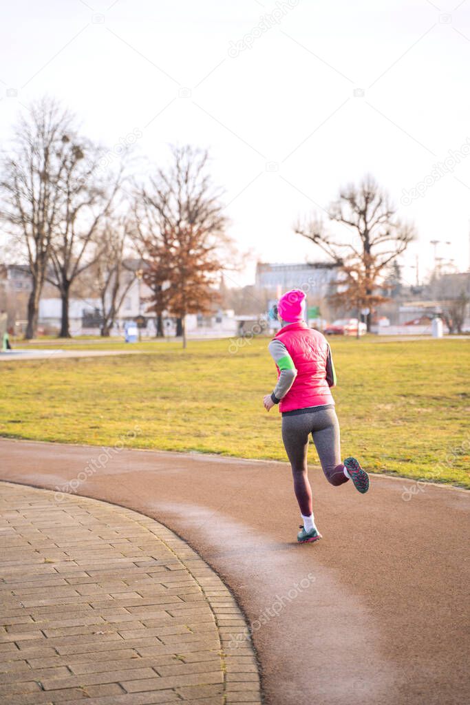 Young fit caucasian woman in fitness clothes running on track in park on sunrise