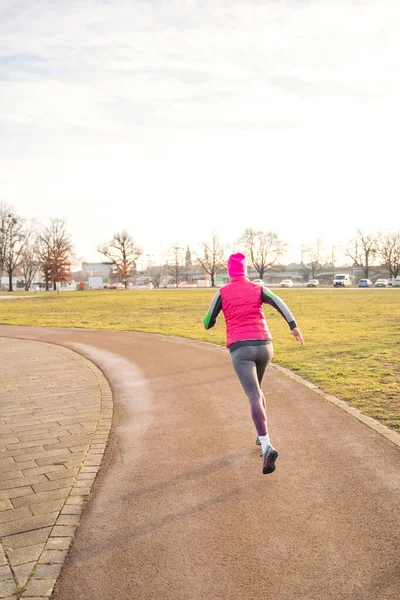 Mujer caucásica en forma joven en ropa de fitness corriendo en pista en el parque en la salida del sol — Foto de Stock