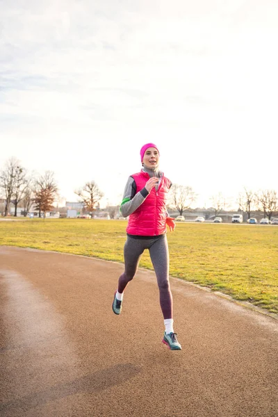 Mujer caucásica en forma joven en ropa de fitness corriendo en pista en el parque en la salida del sol — Foto de Stock