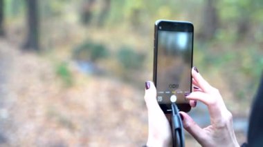 Young woman takes photos and videos on smart phone recording autumnal park