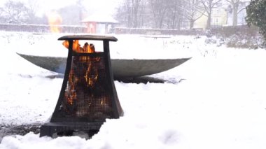 Metallic heater wooden campfire in snowy park on cloudy winter calm cozy day