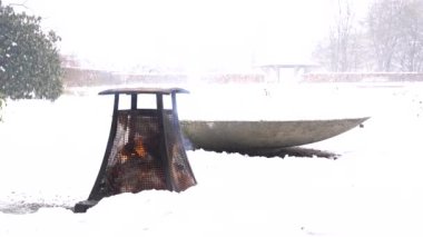 Metallic heater wooden campfire in snowy park on cloudy winter calm cozy day